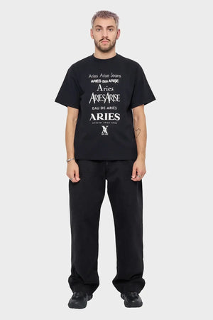 Mężczyzna w czarnej koszulce Aries z białym nadrukiem, czarne spodnie i buty, na jasnym tle