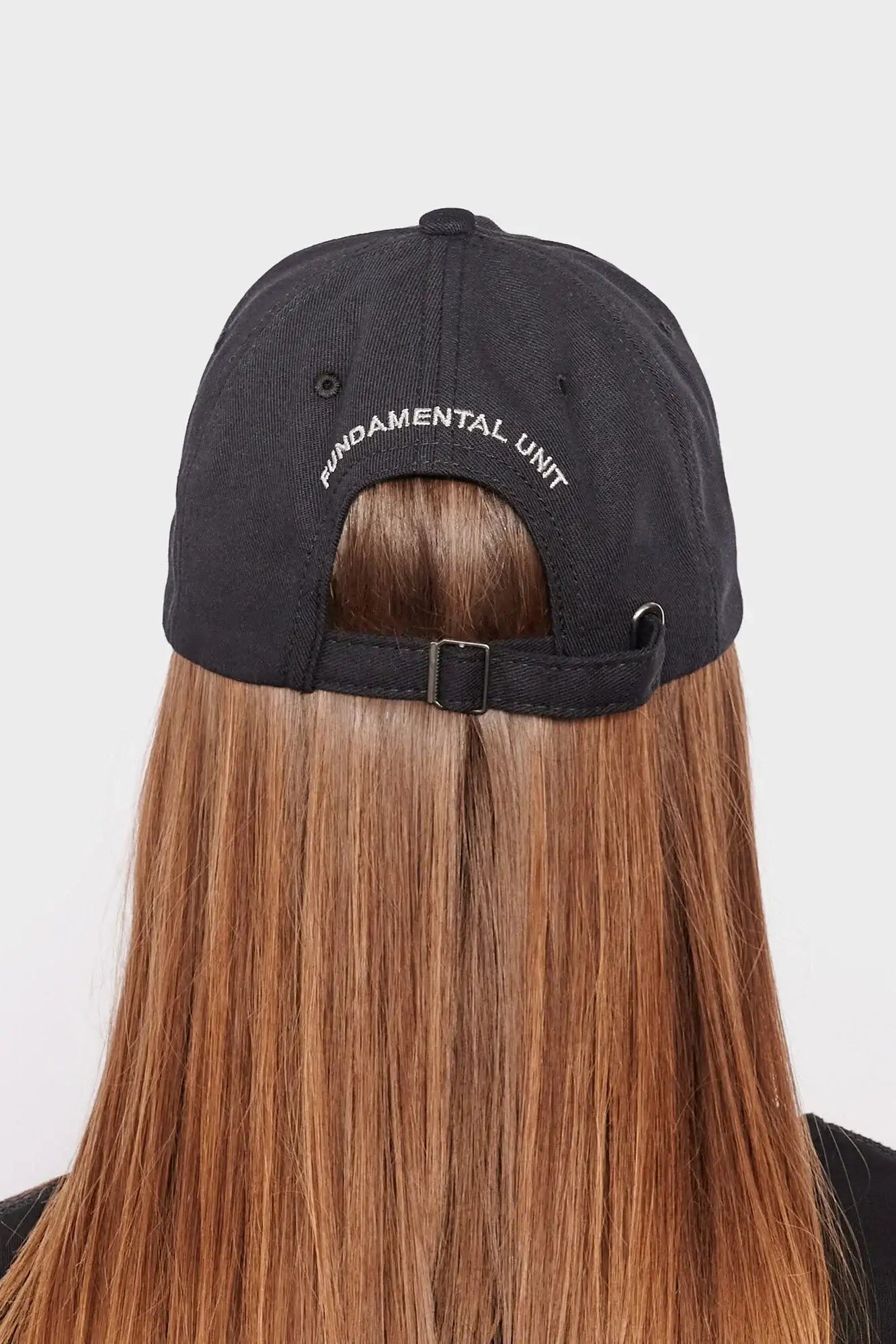 Czarna czapka z daszkiem z napisem FUNDAMENTAL UNIT na tyle, długie proste włosy, styl streetwear