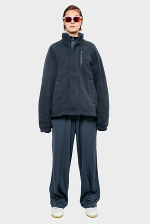 Modelka w ciemnoszarej polarowej kurtce, szerokich spodniach i sportowych okularach, styl streetwear