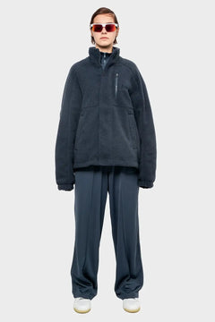 Modelka w ciemnoszarej polarowej kurtce, szerokich spodniach i sportowych okularach, styl streetwear