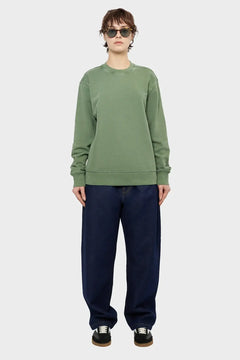 Osoba w zielonej bluzie, ciemnych szerokich jeansach i okularach przeciwsłonecznych, styl streetwear