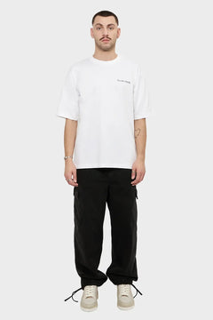 mężczyzna w białym t-shircie z napisem, czarnych spodniach cargo i białych sneakersach, styl streetwear