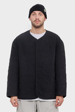 Mężczyzna w czarnej pikowanej kurtce i czarnej czapce na białym tle, minimalistyczna moda streetwear.