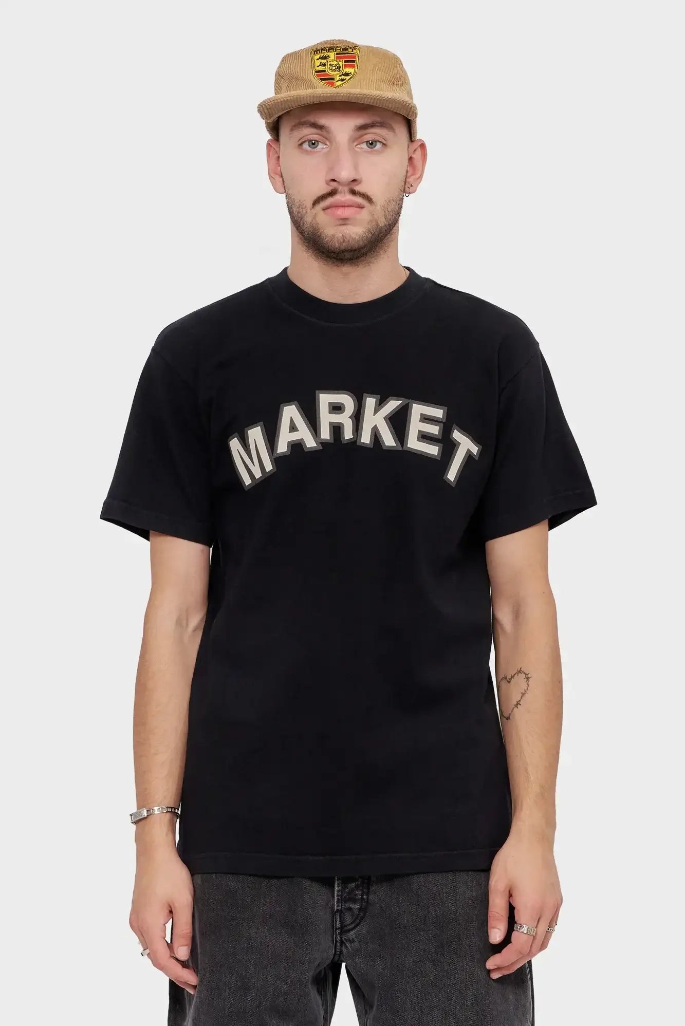 Mężczyzna w czarnej koszulce z napisem MARKET i beżowej czapce z naszywką, moda streetwear