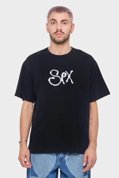 Mężczyzna w czarnej koszulce z białym napisem, styl streetwear, jeansy, minimalistyczne tło