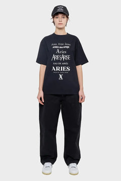 Modelka w czarnej czapce, t-shircie Aries z białym nadrukiem i czarnych spodniach, styl streetwear