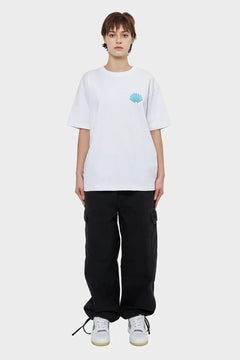 Modelka w białym t-shircie z niebieskim nadrukiem muszli, czarne spodnie cargo, sneakersy