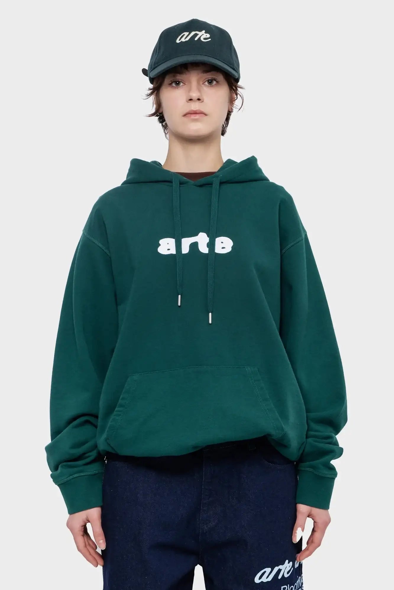 Modelka w zielonej bluzie z kapturem i czapce z napisem arte, modna odzież streetwear.