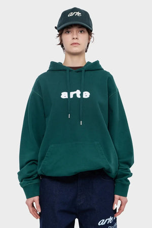 Modelka w zielonej bluzie z kapturem i czapce z napisem arte, modna odzież streetwear.