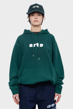 Modelka w zielonej bluzie z kapturem i czapce z napisem arte, modna odzież streetwear.