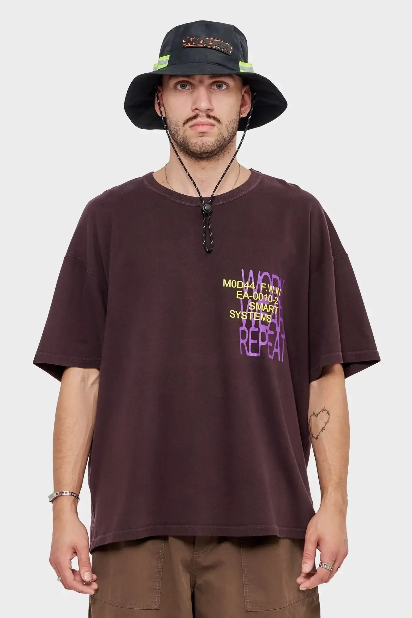 Mężczyzna w brązowej koszulce z nadrukiem MOD44, bucket hat, styl streetwear.