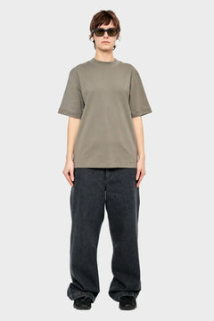 Osoba w luźnym szarym t-shircie, szerokich czarnych jeansach i okularach przeciwsłonecznych, styl streetwear.