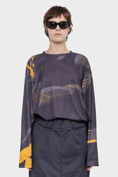 Modelka w ciemnych okularach przeciwsłonecznych, bluzie z długim rękawem z abstrakcyjnym wzorem w odcieniach szarości i żółci, modna odzież streetwear.