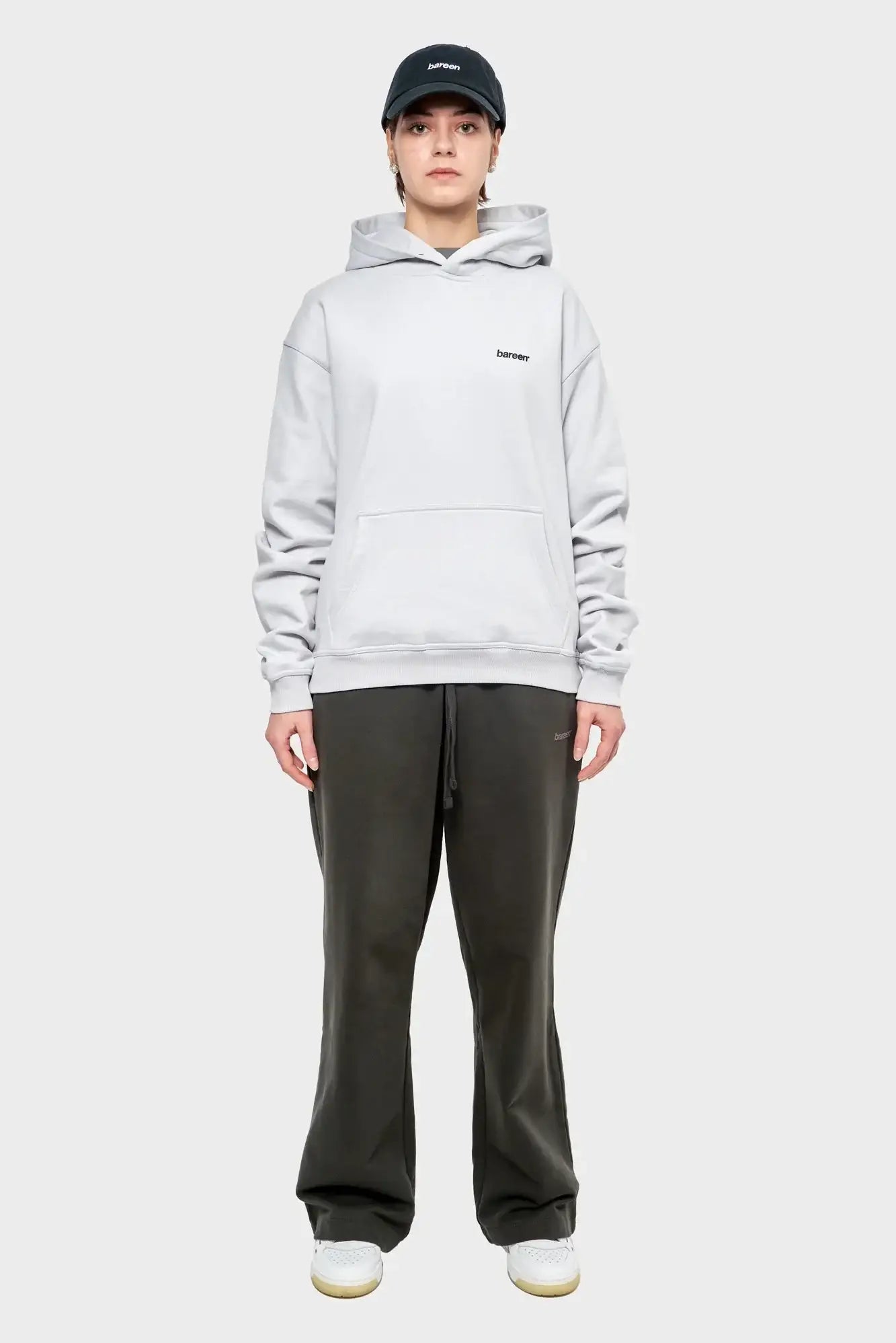 Modelka w jasnej bluzie z kapturem, czarnej czapce i ciemnych spodniach dresowych, look streetwear