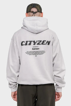 Mężczyzna w szarej bluzie z kapturem z dużym napisem CITYZEN na plecach, luźna odzież streetwear