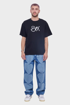 Mężczyzna w czarnym t-shircie z białym napisem i niebieskich jeansach z sercami