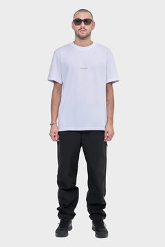 Mężczyzna w białej koszulce ROTDIVISION, czarne spodnie, ciemne okulary, styl streetwear.