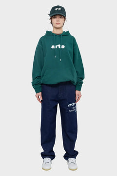 Modelka w zielonej bluzie z kapturem, czapce z daszkiem i granatowych jeansach z nadrukiem, styl streetwear