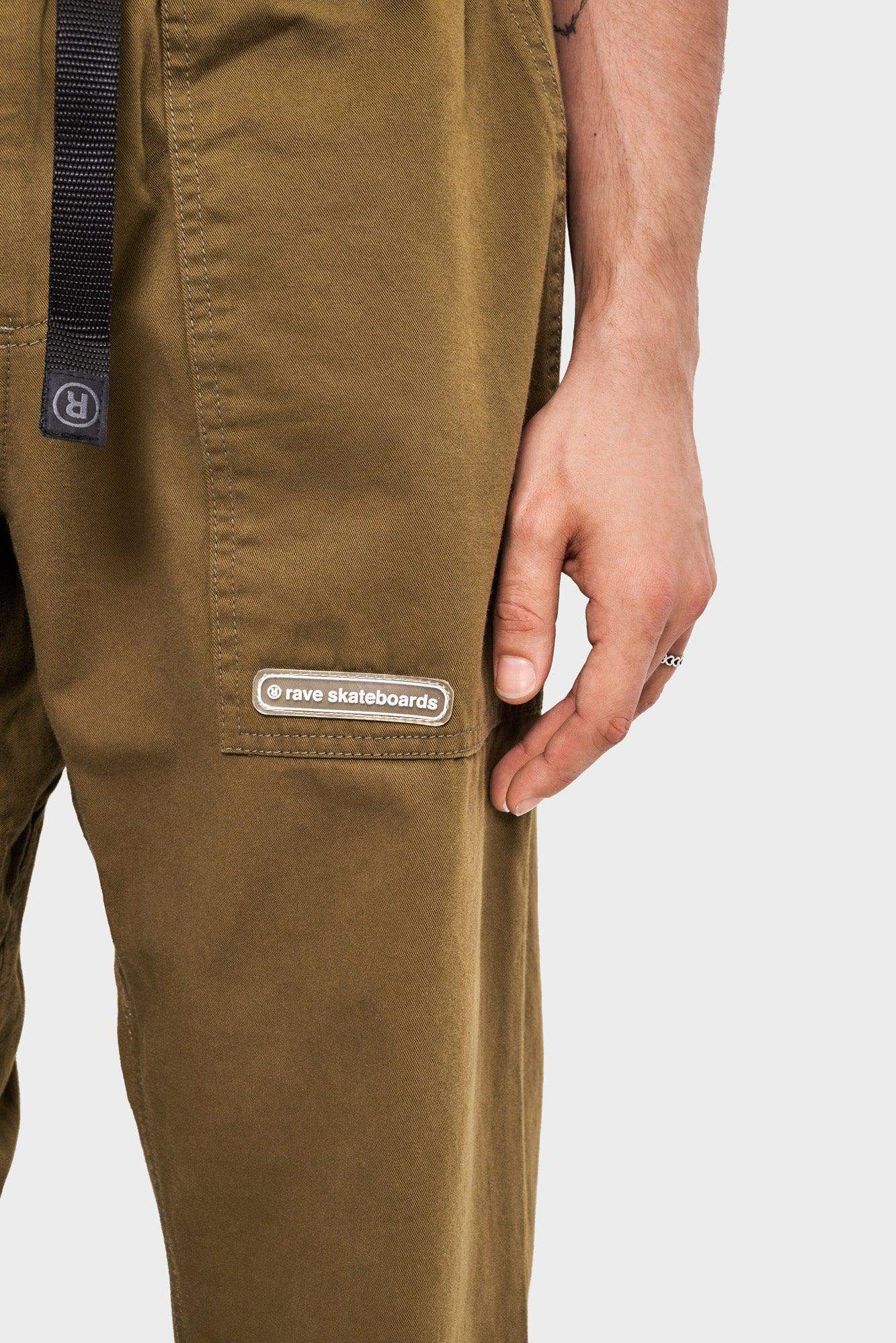 Zielone spodnie cargo rave skateboards z kieszenią i widocznym logo, męska dłoń obok