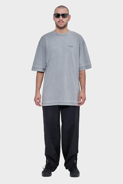 Mężczyzna w szarym oversize t-shircie z napisem SILENCE, czarnych luźnych spodniach i okularach przeciwsłonecznych