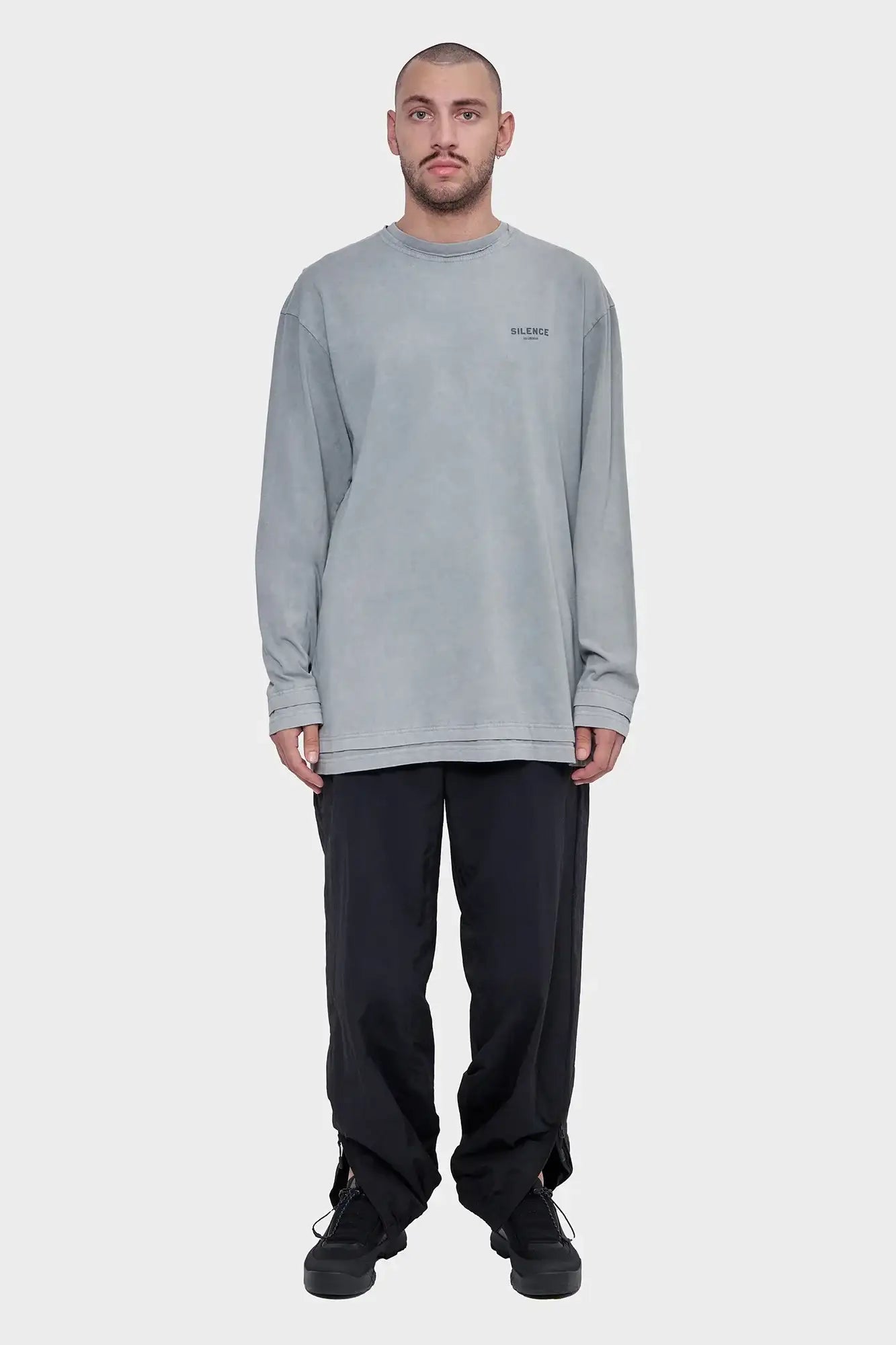 Model w szarym longsleeve z napisem Silence, czarne spodnie, sneakersy, minimalistyczny styl uliczny