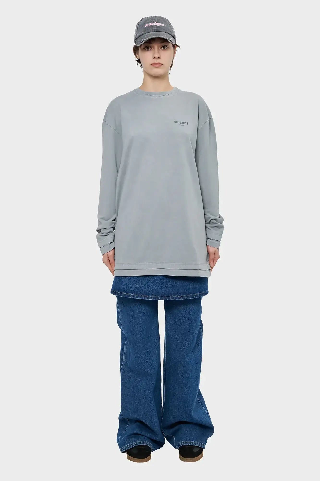 Osoba w szarej bluzie z napisem SILENCE, szerokich jeansach, czapka z daszkiem, styl streetwear.