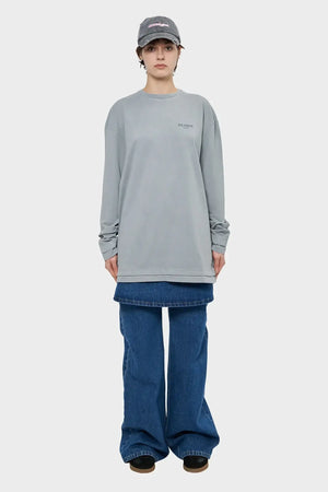 Osoba w szarej bluzie z napisem SILENCE, szerokich jeansach, czapka z daszkiem, styl streetwear.