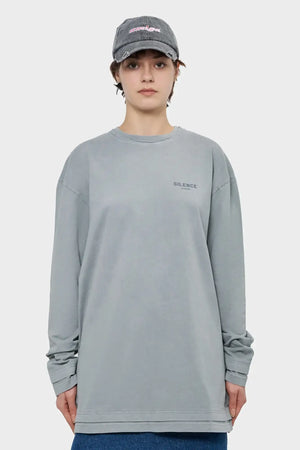 Osoba w szarej bluzie z napisem 'SILENCE' i czapce z daszkiem na jasnym tle, moda streetwear.