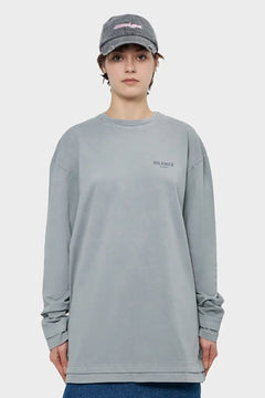Osoba w szarej bluzie z napisem 'SILENCE' i czapce z daszkiem na jasnym tle, moda streetwear.