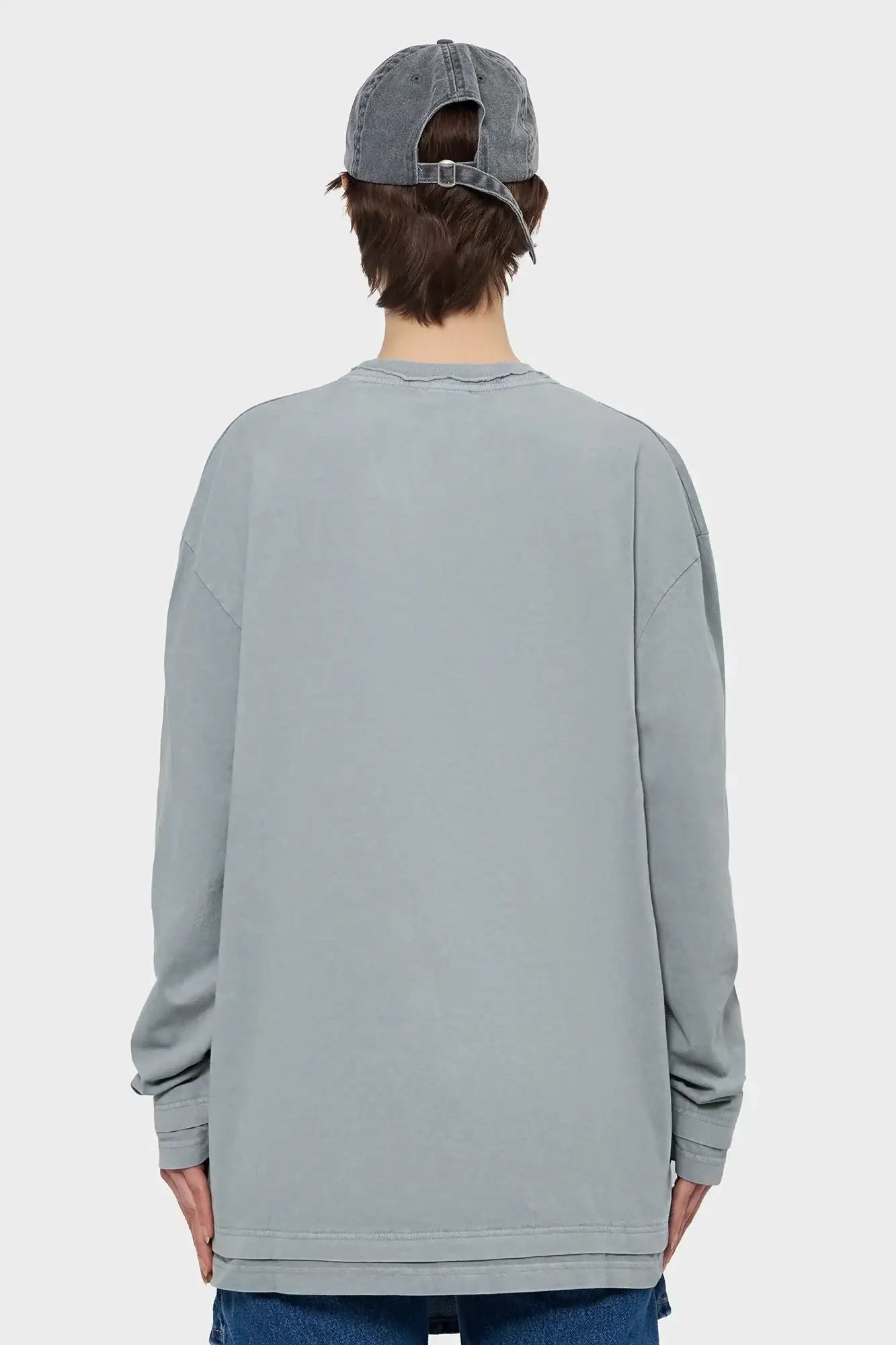 Szara bluza oversize z długim rękawem, model z tyłu, jeansowa czapka, styl streetwear