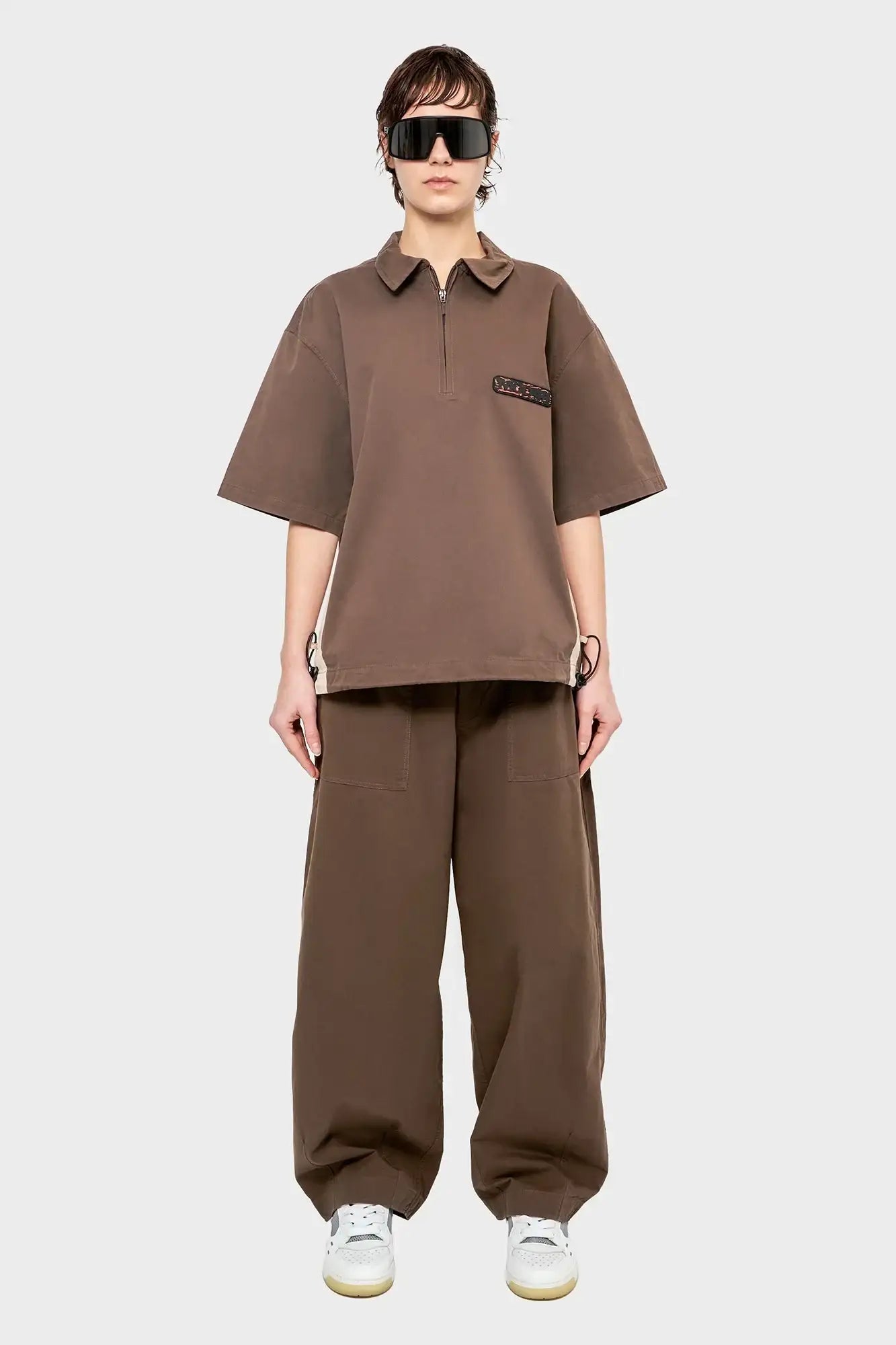 Modelka w brązowym oversize komplecie streetwear, szerokie spodnie, okulary, białe sneakersy