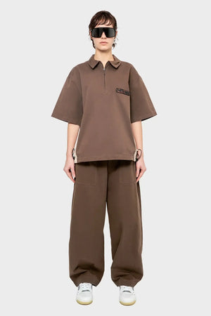 Modelka w brązowym oversize komplecie streetwear, szerokie spodnie, okulary, białe sneakersy