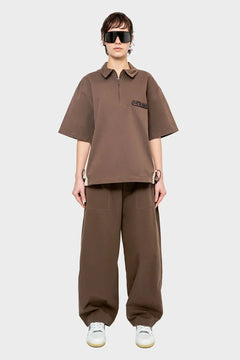 Modelka w brązowym oversize komplecie streetwear, szerokie spodnie, okulary, białe sneakersy