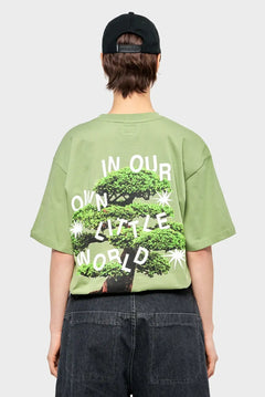 Zielony t-shirt z nadrukiem drzewa bonsai i napisem IN OUR OWN LITTLE WORLD, czapka z daszkiem