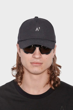 Mężczyzna w czapce z daszkiem A1, ciemnych okularach i czarnym t-shircie, styl streetwear