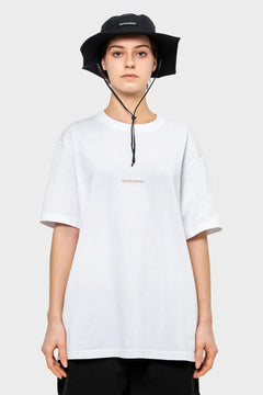 osoba w białym t-shircie RIOTDIVISION i czarnym kapeluszu bucket hat, na jasnym tle