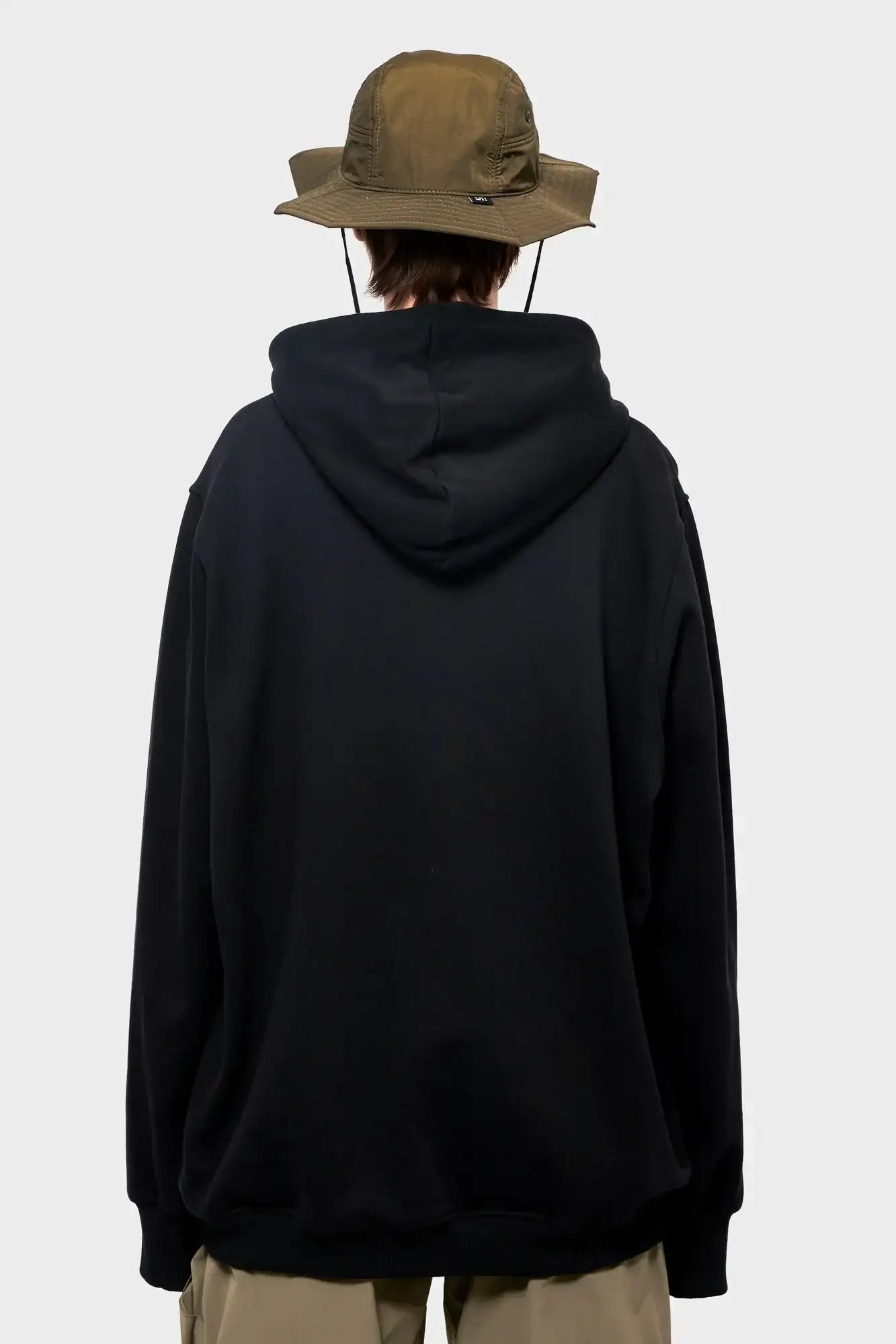 Osoba w czarnej bluzie z kapturem i oliwkowym kapeluszu, widok od tyłu, moda streetwear