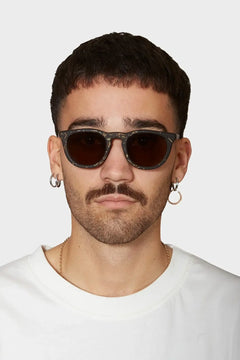 Mężczyzna w okularach przeciwsłonecznych z ciemnymi szkłami, białej koszulce i kolczykami, modny styl streetwear
