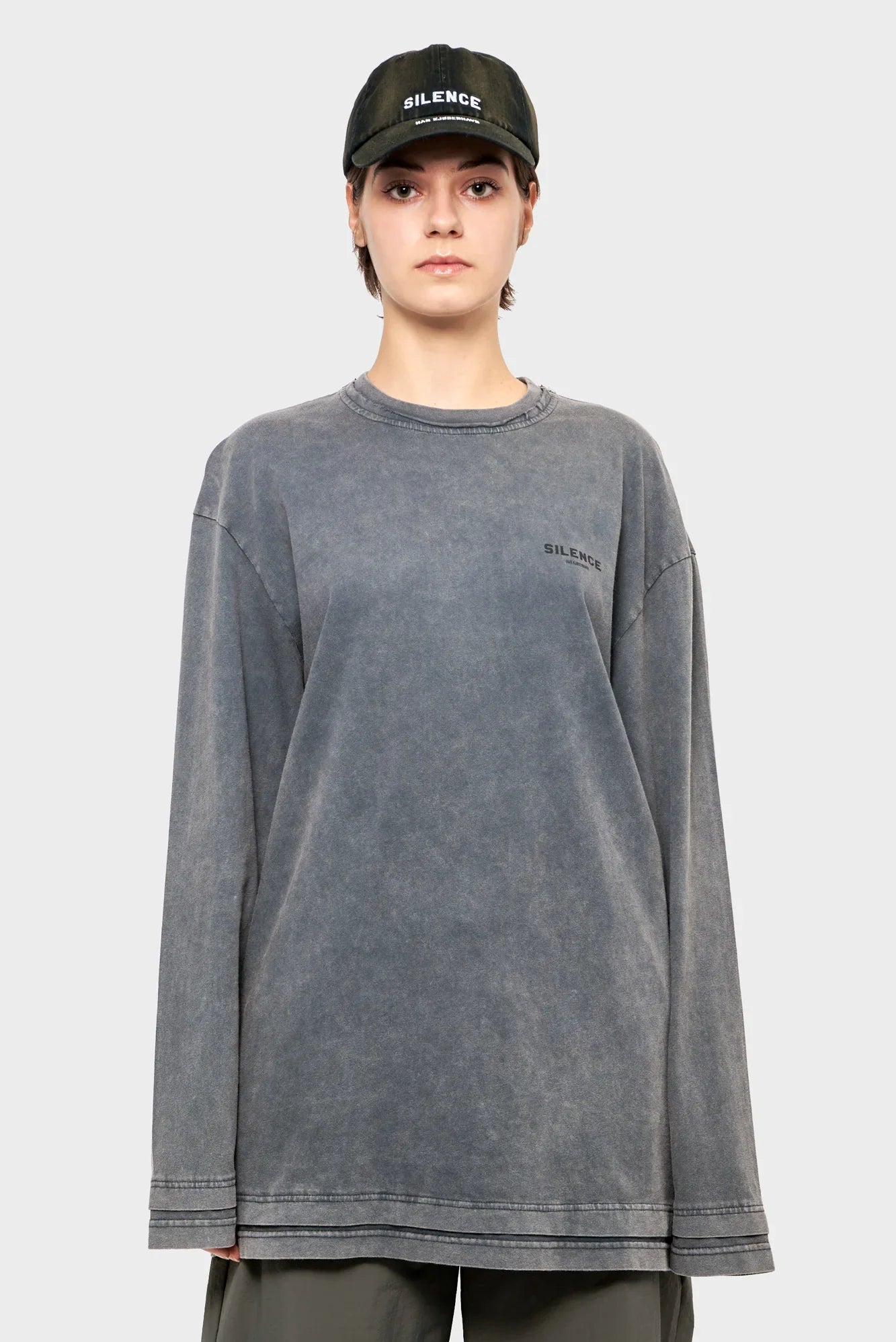 Osoba w czarnej czapce z daszkiem i szarej bluzie z napisem SILENCE, minimalistyczna moda streetwear