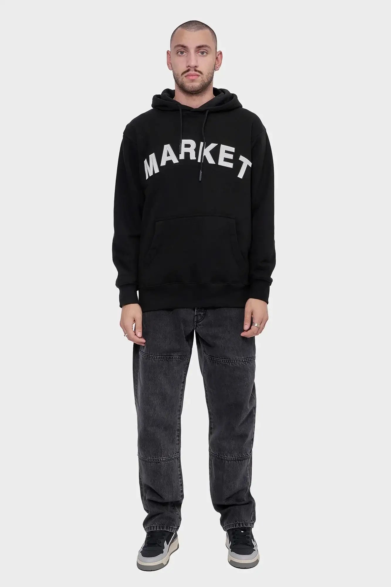 Mężczyzna w czarnej bluzie z kapturem z napisem MARKET, luźne jeansy i sportowe buty