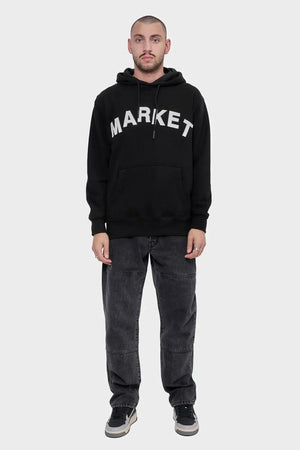 Mężczyzna w czarnej bluzie z kapturem z napisem MARKET, luźne jeansy i sportowe buty