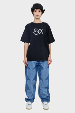 Osoba w czarnym t-shircie z napisem, szerokich jeansach z sercami i czarnym kapeluszu bucket
