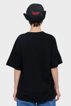 Osoba w czarnej koszulce oversize i ciemnym kapeluszu z napisem, styl streetwear