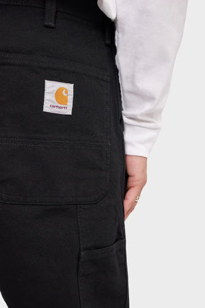 Czarne spodnie robocze Carhartt WIP z kieszenią i logo, biała bluza, detal odzieży
