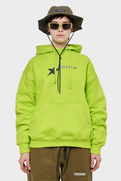 Modelka w limonkowej bluzie z nadrukiem gwiazdy, oliwkowym kapeluszu RIOTDIVISION i okularach, streetwear