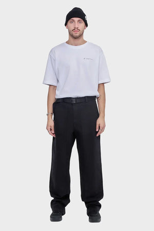 Mężczyzna w białym t-shircie, czarnych szerokich spodniach i czarnej czapce, minimalistyczny streetwear.