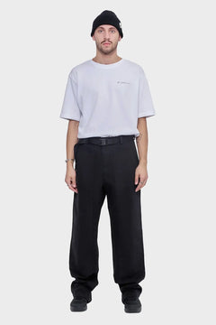 Mężczyzna w białym t-shircie, czarnych szerokich spodniach i czarnej czapce, minimalistyczny streetwear.