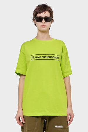 Modelka w limonkowej koszulce rave skateboards, brązowe spodnie, okulary przeciwsłoneczne