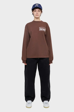 Osoba w brązowej bluzie Aries z logo, granatowej czapce i czarnych spodniach, moda streetwear