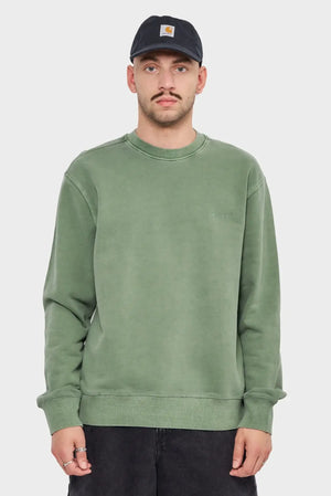 Mężczyzna w zielonej bluzie Carhartt WIP i czapce z logo, neutralne tło, odzież streetwear